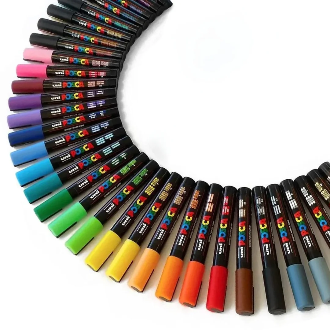Markers and Pens. There are a load of posca markers lines up next to each other in a half circle shape. Spanning from the top of the frame, anti clockwise, around to the right hand side of the frame.