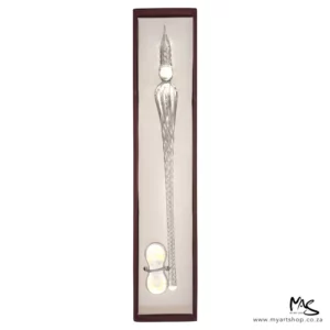 There is a single Glass Dipping Pen Transparent in a box, shown vertically, in the center of the frame. The box is brown, and there is a beige cushioning in the bottom of the box and the pen is sat on the cushioning. There is a clear glass pen rest, placed at the bottom of the pen. The image is on a white background.