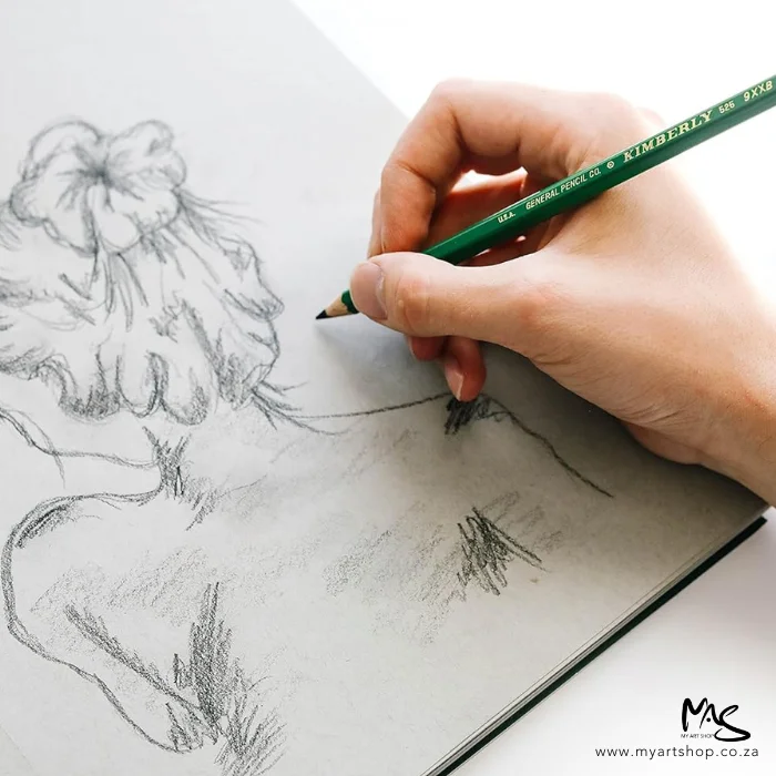 9xxb-kimberley-drawing-pencil-general-pencil-co-06 A persons hand is seen coming out of the right hand side of teh frame, they are holding a 9XXB Kimberley Drawing Pencil from the General Pencil Co. and they are drawing a sketch of the back of a woman on a sketch pad. The image is cut off by the frame.