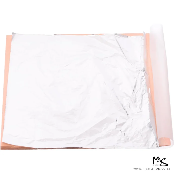 mont-marte-imitation-silver-leaf-04 An open pack of Mont Marte Imitation Silver Leaf can be seen in the center of the frame. The sheets are silver and there is a peach coloured paper between the sheets. The image is on a white background.
