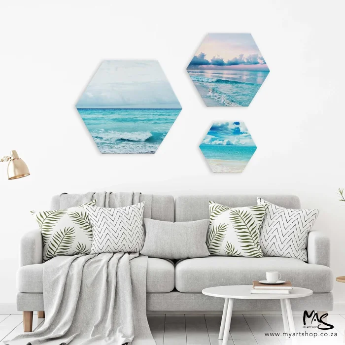 dala-hexagonal-stretched-canvas-04 There are three Dala Hexagonal Stretched Canvases hanging on a wall behind a couch that has cushions and a blanket thrown over it. The canvases have pictures of an ocean theme.