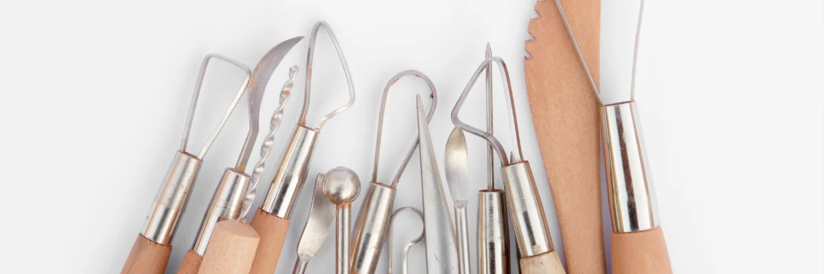 Doughn’t Worry Pottery Tools That Will Transform Your Clay Game shows a range of different pottery tools in the center of the image. they all have brown handles and metal tops of different shapes and sizes. there is one flat paddle on the right hand side. they are all facing upwards from the bottom of the image. they are on a white background