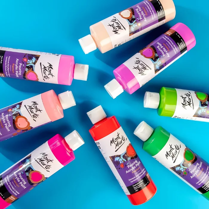 mont-marte-pouring-acrylic-paint-06 There are 8 bottles of different coloured Mont Marte Pouring Acrylic Paints shown laying on their sides on a bright blue surface. They are lying randomly in the frame.