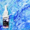 A bottle of Mont Marte Premium Silicone Oil is shown along the left hand side of the frame. The bottle is white plastic with a label around the body of the bottle that is printed with text and the Mont Marte Logo. The bottle has a nozzle top and cap. The bottle is shown over laying a background of blue paint that has been poured and cells have created.