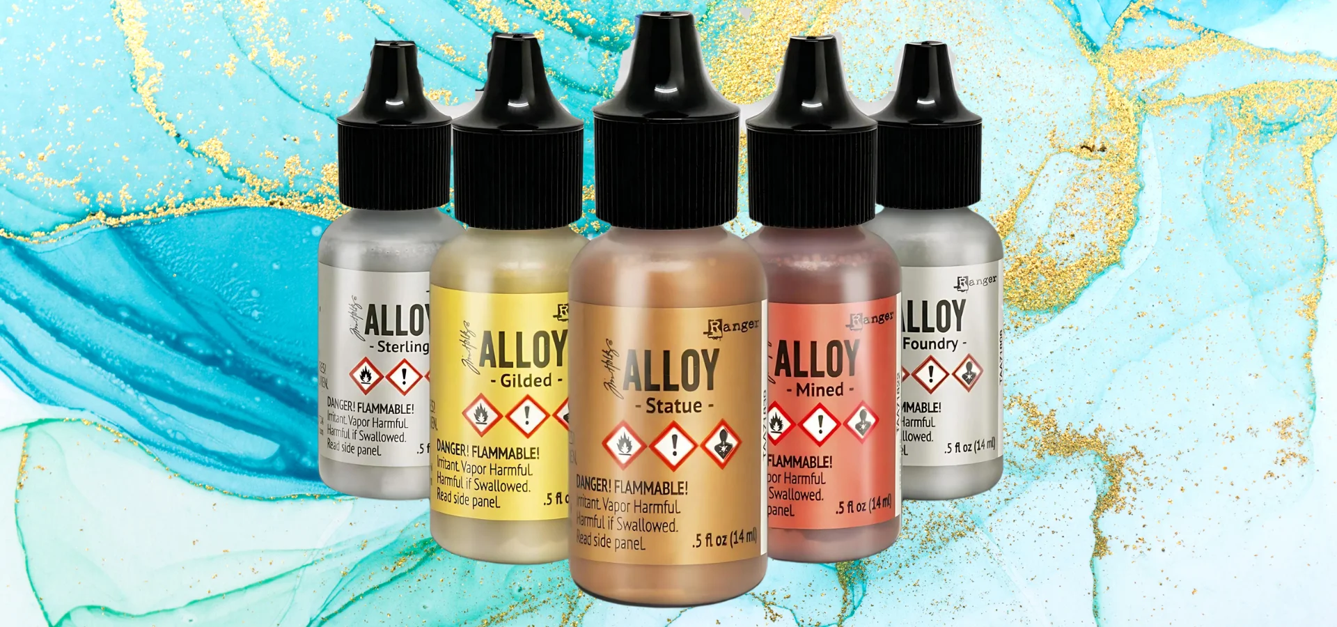 alcohol-ink-alloys-crafting-wizardry shows in the image the alloy bottles standing forawrd facing in the center of the image. they are standing in a v pattern. there are five bottles. they are clear bottles showing the colour that is inside of them which are all metallic colours of silver snad gold, coppers and rose golds. they all have black pointed nozzle lids. they are sitting on a blue alcohol ink background. that is shades of a cerulean type blue with the gold alloy inside of it giving a gold leafing look.