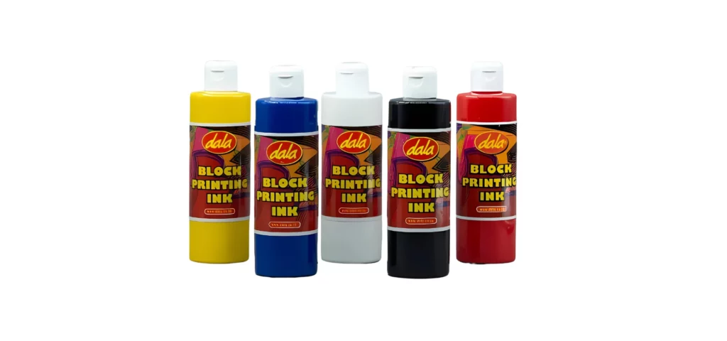 dala-block-printing-inks-demystified shows in this image a row of the dala inks . from left to right. yellow, blue, white, black and then red. all are clear bottles showing the colour inside of them. their caps are white and their labels are in the center of the bottle and wrap all the way around. they are on a white background