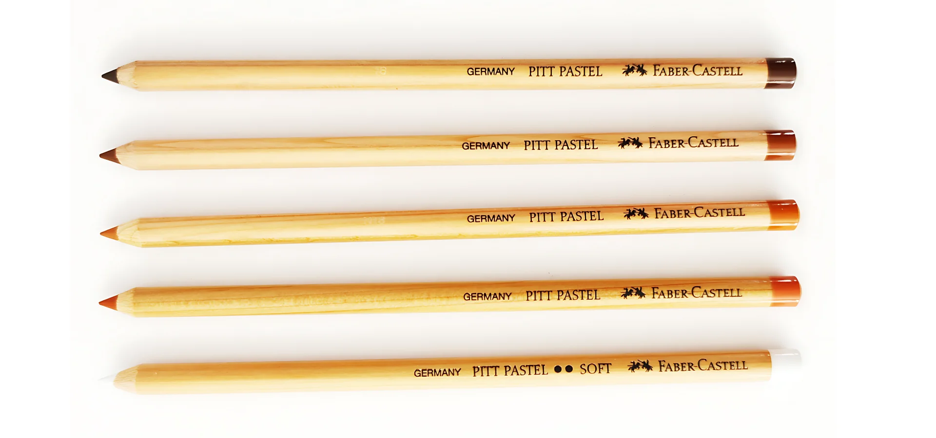 Faber-Castell Pitt Pastel Pencils Unveiled are in the image. the pencils are lying horizontally across the image. the nibs are facing the left side of the image. they are brown cased wood pencils. they have black writing on them with the brand name and product name viable. the ends of them are different shades of brown and white showing what colour each pencil is. they are on a white background