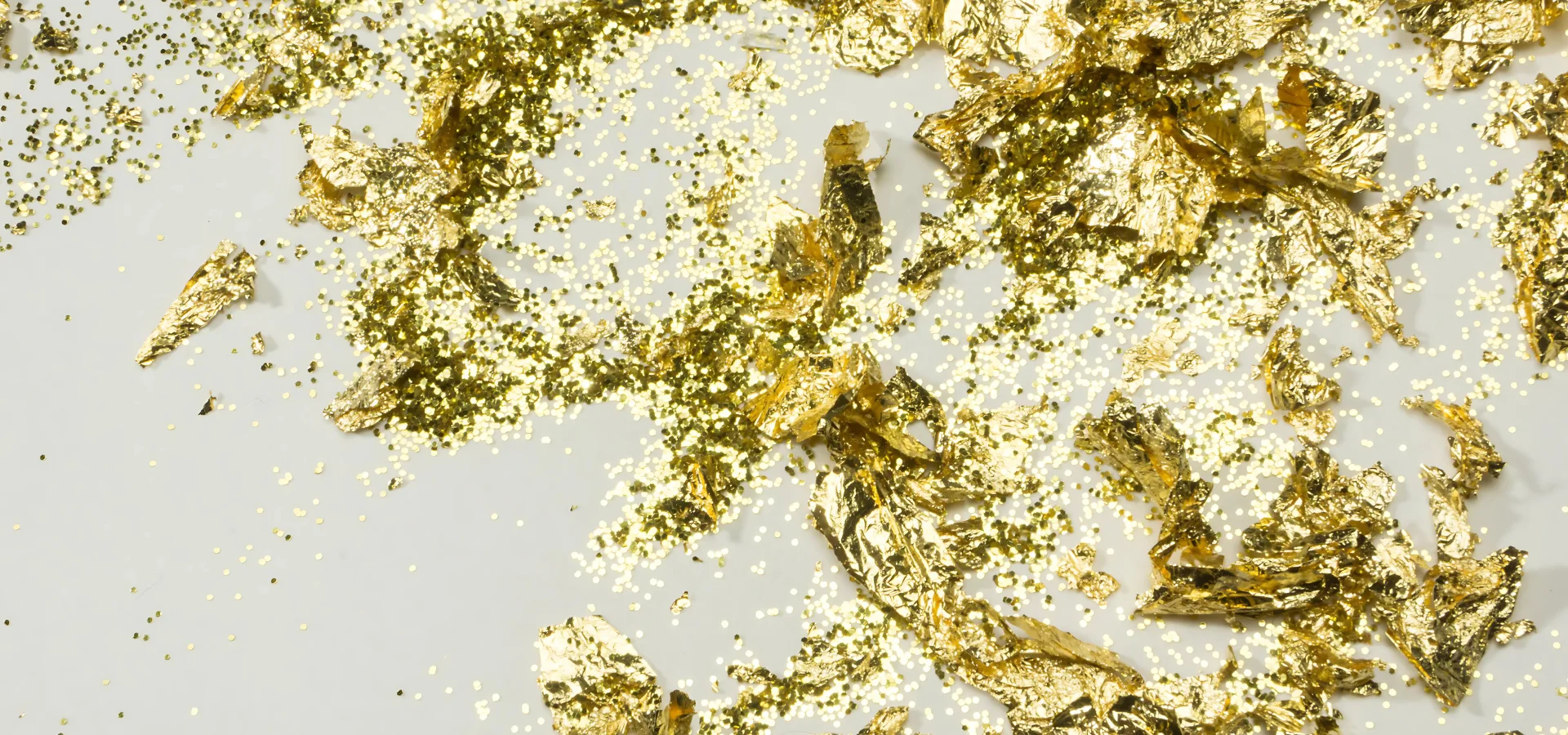 gold-leaf-create-your-gilded-masterpiece. is showing in the image gold leaf that is broken and scattered around all across the image. some flakes are tiny and some are larger. it is a brilliant bright gold colour. on a white background