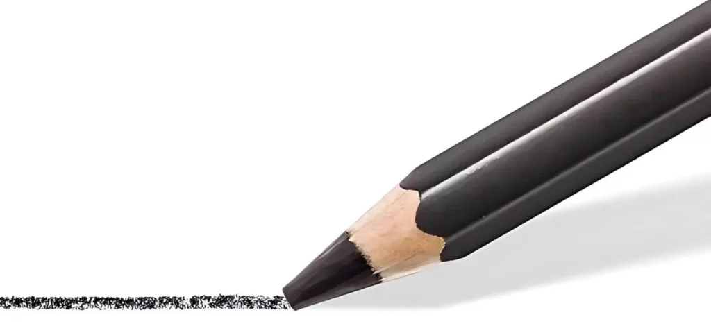 Staedtler Mars Lumograph Black Pencil. A close up of the pencil tip. The pencil is coming in from the right hand side of the frame and is at a slight angle. The pencil is cut off by the right hand side of the frame. The pencil appears to have drawn a line in front of it, which extends to the left hand side of the frame. The wooden pencil has a black barrel and black lead. The image is center of the frame and on a white background.