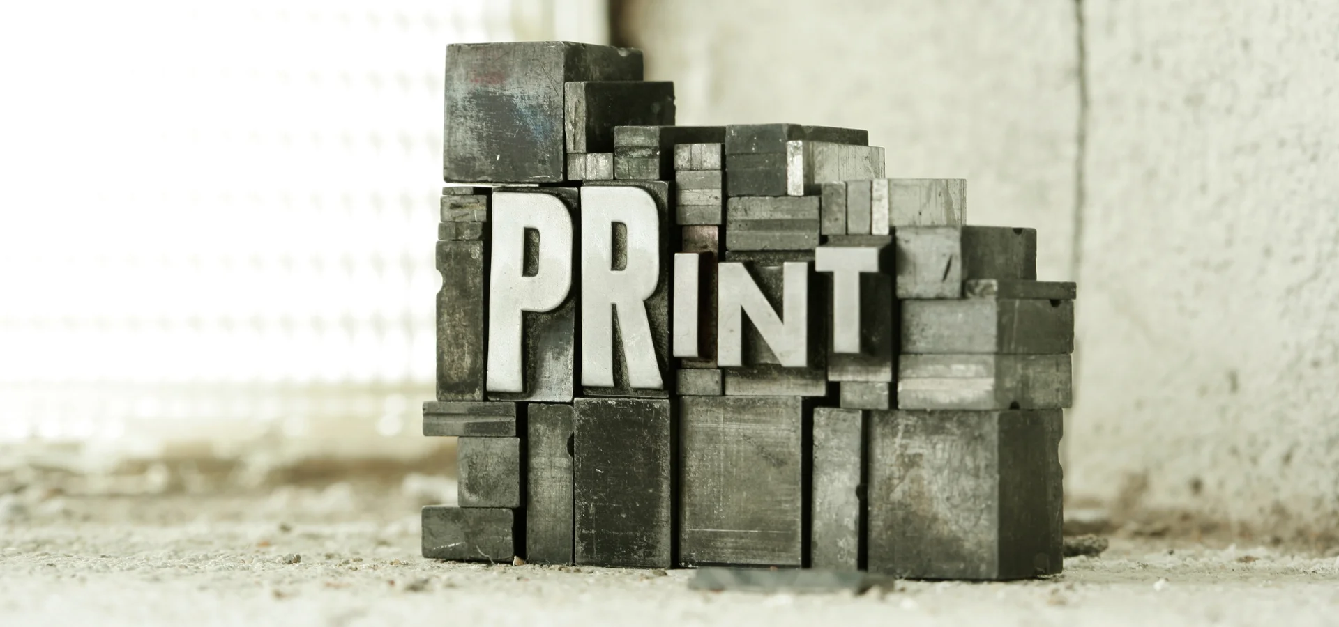 speedball-block-inks-unleashing-your-inner-picasso. in the center of this image are wooden stamping block letters that spell out the word print in different sized letters. the image is in a sepia vintage tone and is angled slightly to the left facing side. the background is a blurred room behind the blocks