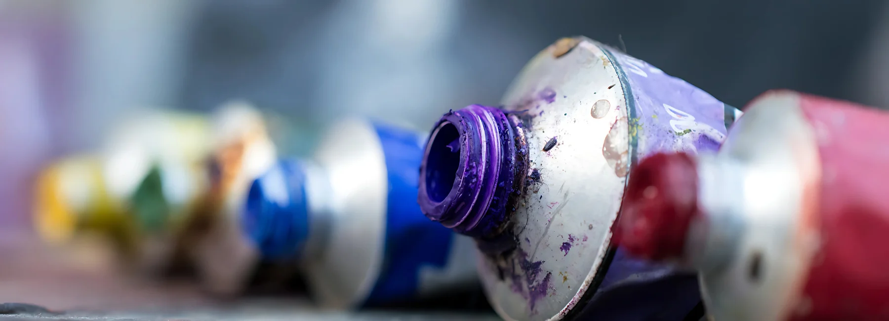 daler-rowney-georgian-oil-paint-gearing-up-your-palette. there is a close up image of tubes of oil paunts in the primary colours of blue, red, yellow. there is also a grren. they are all out of focus except the second paint which is a blue oil paint. showing the paint around the tip. they have their lids off