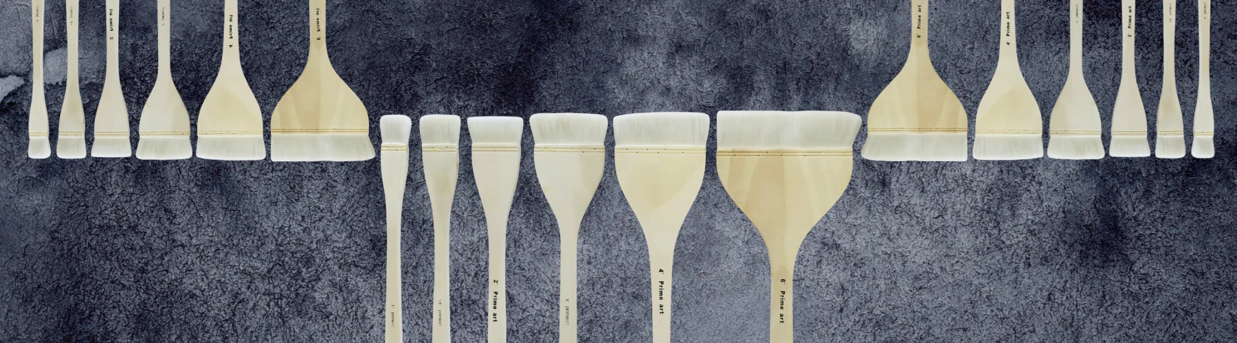 hake-brushes-a-stroke-of-art. the background is a black watercolour wash. there are three sets of six hake brushes. two coming from the top and one set coming from the bottom in the center. they are a light brown wood with white hairs.