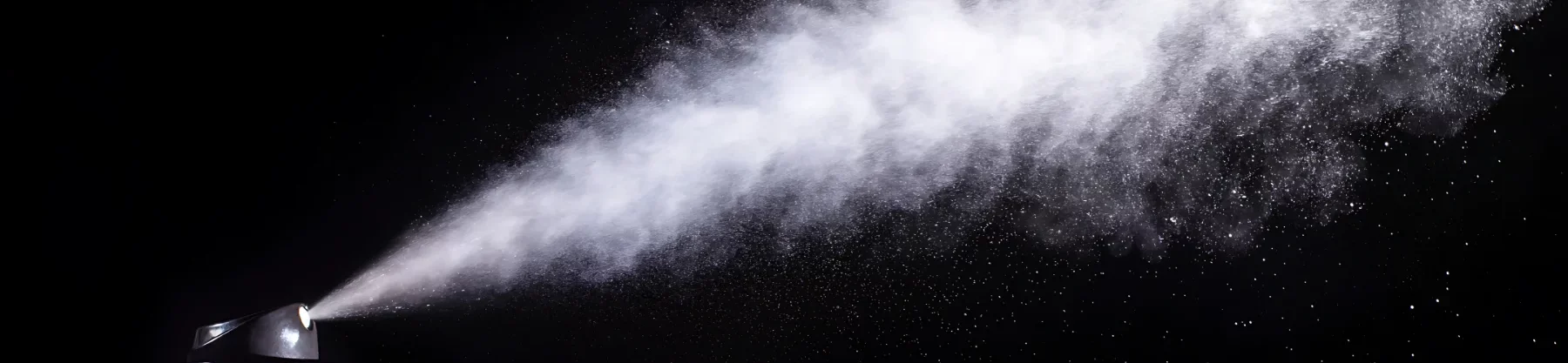 oil-and-acrylic-varnish-the-glossy-guide. from the bottom left corner there is a aeresol can spraying upwards. you can see the spray across the image in a dusting from bottom left to top right hand side. the background is black so as to be able to show the spray properly