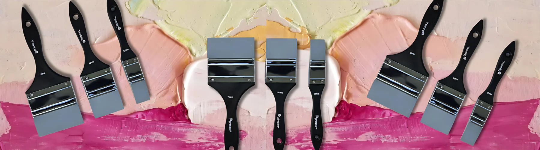 silicone-paint-brushes-adding-fun-to-art. in the background of the image is a textured acrylic paint in the colours of pink, cream and peach. it is thick and stodgy. infront of it are three sets of three silicone brushes. the center one is standing upright and the two on either side are upside down and facing inwards. they have black handles with grey silicone wedges on them