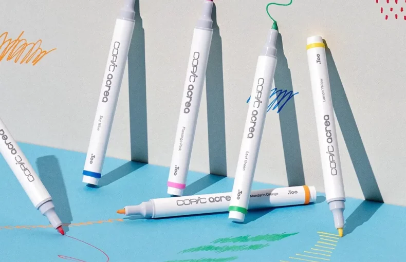 acrea-paint-markers-splash-scribble-create. There are 6 Copic Acrea Paint Markers shown in the frame. They are standing up against a wall that has been drawn on using the markers.