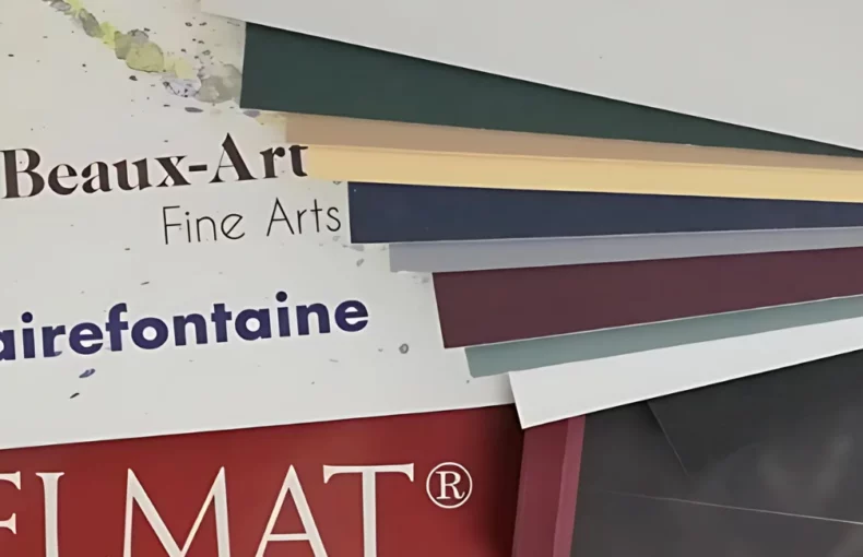clairefontaine-pastelmat-creating-colourful-masterpieces. the image is a close up of the pastel mat paper. there are two pads on the left and you can see their covers and on the right are the single sheets of the paper fanned out to show the different colours of them