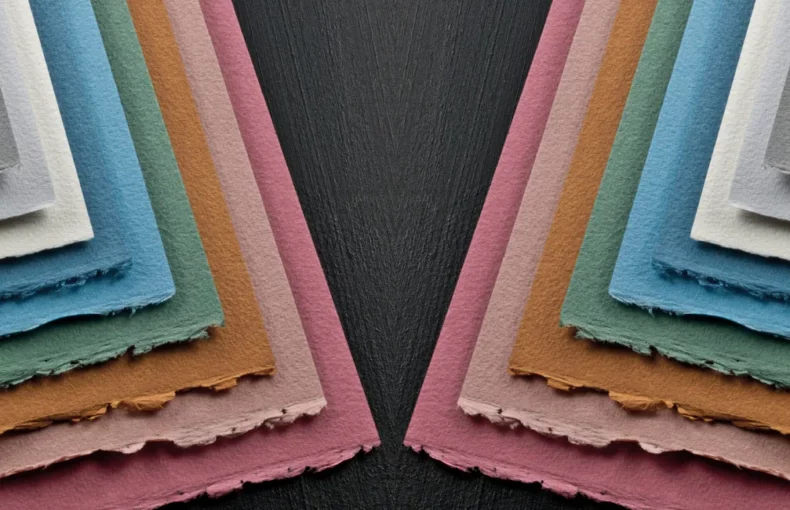 fabriano-cromia-paper-delve-into-artistry. the image is of a mirror image of the same picture of various colours of the cromia paper fanned out to show the different colours and coming from the outer edge going in. on a dark wood table top