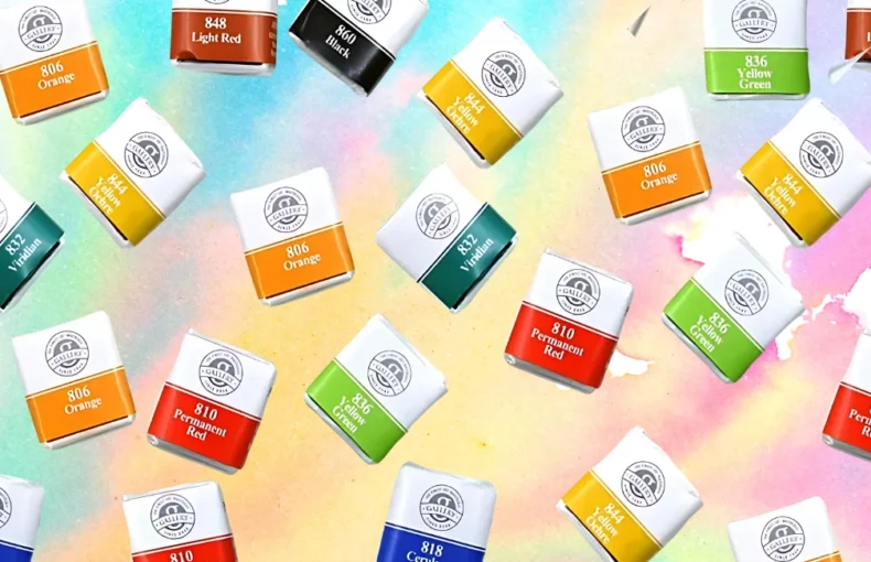 mungyo-watercolour-half-pans-revamp-your-artistry. the background of the image is a watercolour done in pastel shades of blue, pink, yellow and green. done in a wash. infront of that are many pans of the mungyo watercolour paint scattered around haphazardly across the image. the pans are small square white containers with a paper covering them showing the colour of the paint and the name written on that in white