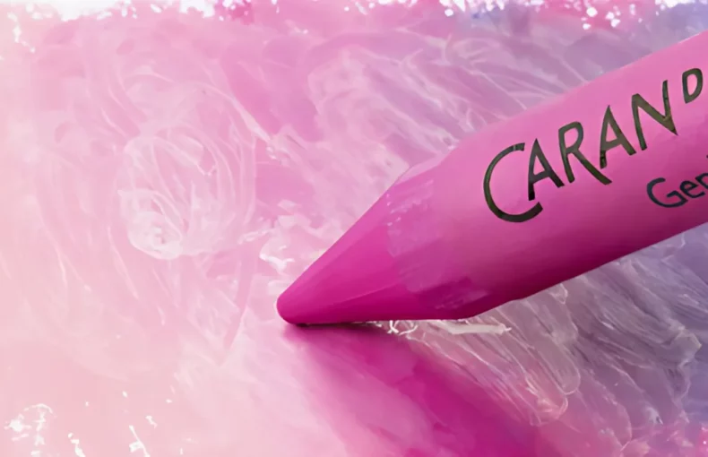 neocolor-ii-pastels-colour-explosion. the image is a close up of one neo colour crayon. it is pink and has the name caran dache written in black on it. it is drawing on the paper and shading out between purple and pink and there is a large ovalish area where it has coloured in. the background is white.
