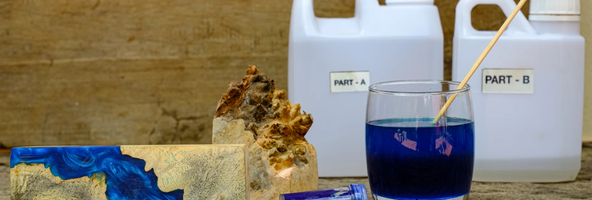 resin-casting-shine-bright-like-a-diamond. the image shows two large containers of resin on the right hand side and a jar infront with blue liquid in it and bricks on the left hand side that have it poured over them creating arty effecrs. infront of a wooden wall