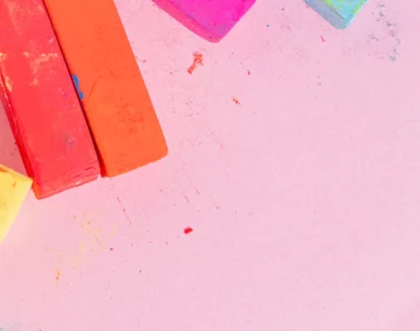 tiziano-pastel-paper-pads-creative-vibes-only. the image shows soft pastels on the left hand side of the image in various colours. orange, yellow, blue and pink. the background is light pink fabriano pastel paper.