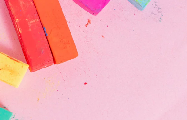 tiziano-pastel-paper-pads-creative-vibes-only. the image shows soft pastels on the left hand side of the image in various colours. orange, yellow, blue and pink. the background is light pink fabriano pastel paper.