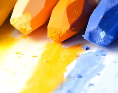 water-soluble-pastels-for-art-enthusiasts. the image shows a close up of a variety of different colours of oil pastels that are at the top of the image. they have their own colour laid down on the paper infront of them. they are in a rainbow colour order and are brightly coloured pastel sticks