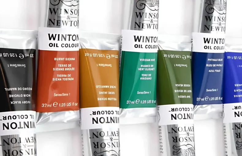 winsor-and-newton-winton-oil-paint-the-power-of-precision. in the center of the image are 10 tubes of winsor and newton winton oil paint. they are lying 5 facing up and 5 facing down. the colours blocks on the tubes all line up and they are in a rainbow colour order. they are on a white background. they have silver tubes, with a thich colour band that shows the colour inside the tube and black writing on them